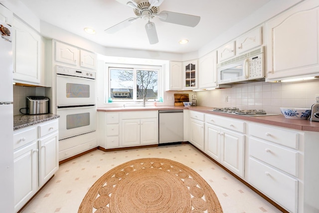 kitchen with white appliances, a sink, white cabinets, backsplash, and ceiling fan