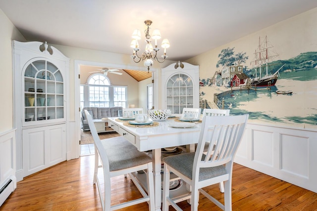 dining space with light wood-type flooring, a baseboard radiator, a chandelier, wainscoting, and ceiling fan