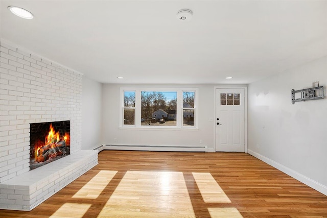 foyer entrance with a brick fireplace, a baseboard heating unit, and light wood-type flooring