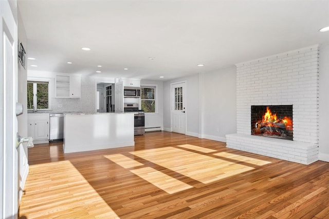 unfurnished living room featuring a brick fireplace, baseboard heating, and light hardwood / wood-style flooring