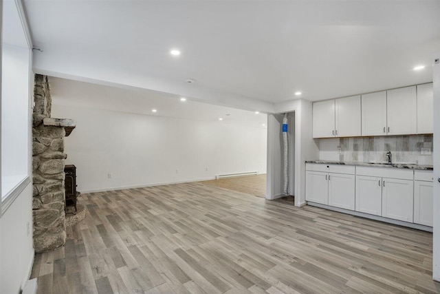 unfurnished living room featuring sink, light hardwood / wood-style floors, a wood stove, and baseboard heating