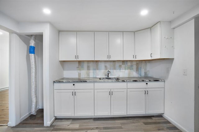 kitchen with sink, backsplash, white cabinets, and hardwood / wood-style flooring