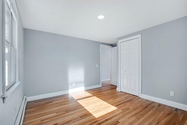 unfurnished bedroom featuring a baseboard radiator, light hardwood / wood-style floors, and a closet