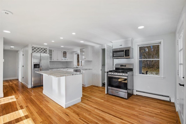 kitchen featuring tasteful backsplash, white cabinetry, a center island, baseboard heating, and stainless steel appliances