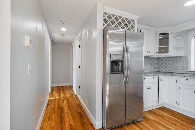 kitchen with light hardwood / wood-style flooring, light stone counters, white cabinets, stainless steel fridge with ice dispenser, and decorative backsplash