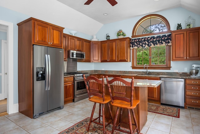 kitchen featuring appliances with stainless steel finishes, light tile patterned floors, a kitchen island, a breakfast bar, and vaulted ceiling