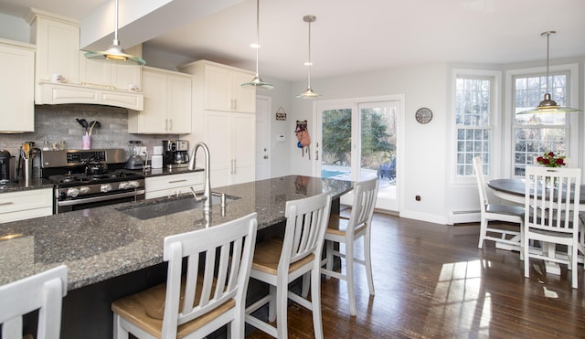 kitchen with decorative backsplash, a sink, stainless steel gas range oven, and dark stone countertops