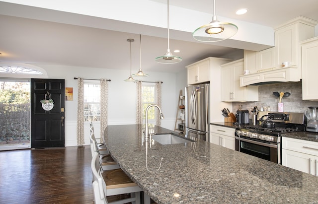 kitchen featuring stainless steel appliances, dark stone counters, a sink, and a kitchen bar