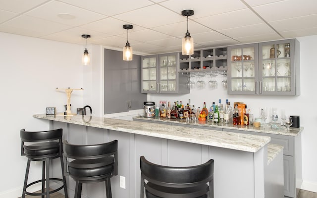 bar featuring wet bar, baseboards, a drop ceiling, and decorative light fixtures