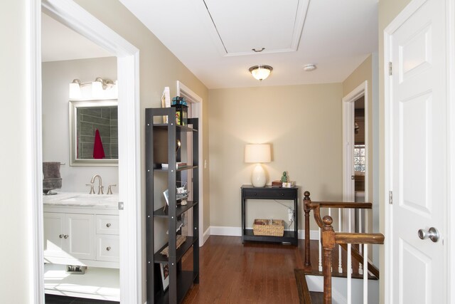 corridor with attic access, baseboards, dark wood-style flooring, and a sink