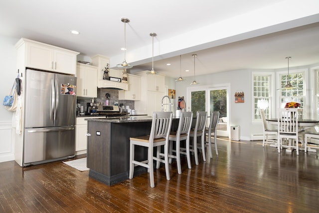 kitchen with appliances with stainless steel finishes, an island with sink, decorative light fixtures, and white cabinetry