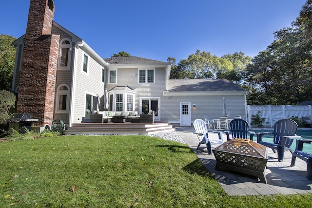 back of property featuring a chimney, an outdoor living space with a fire pit, a lawn, and fence