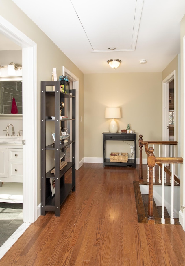 hallway featuring a sink, dark wood finished floors, attic access, and baseboards