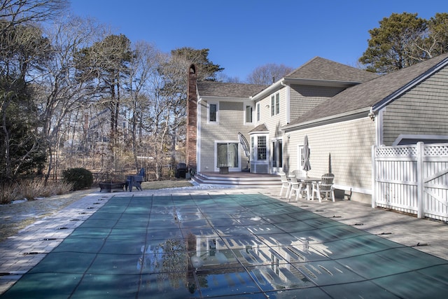 back of house with entry steps, a patio, a covered pool, a chimney, and fence