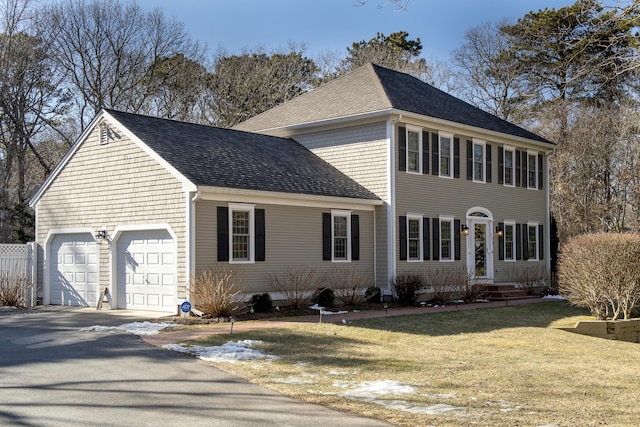 colonial-style house featuring a garage, a front yard, a shingled roof, and driveway