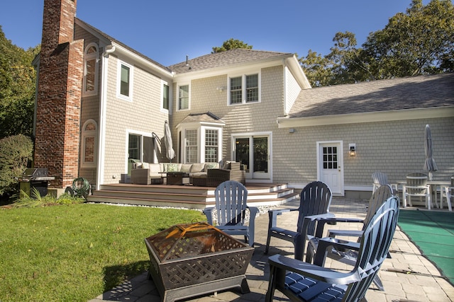 back of property with a patio, a shingled roof, a lawn, a chimney, and an outdoor living space with a fire pit