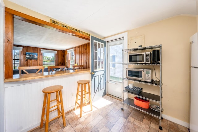 1006 Craigville Beach Rd Unit 4, Centerville, MA 02632 - kitchen with stainless steel microwave, wooden walls, baseboards, stone finish flooring, and a kitchen bar