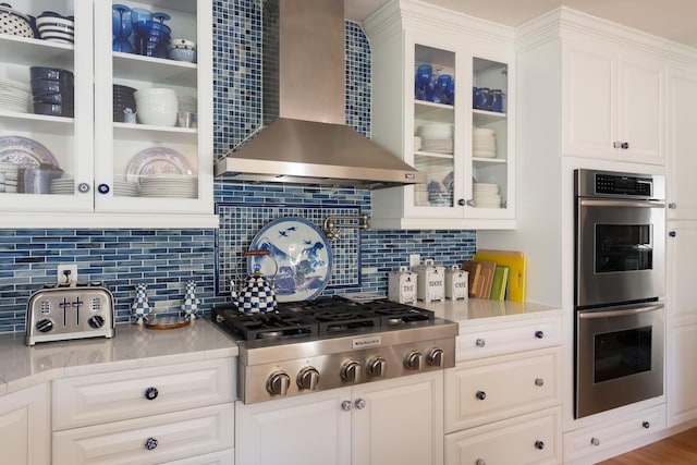 kitchen featuring appliances with stainless steel finishes, white cabinets, light countertops, and wall chimney range hood