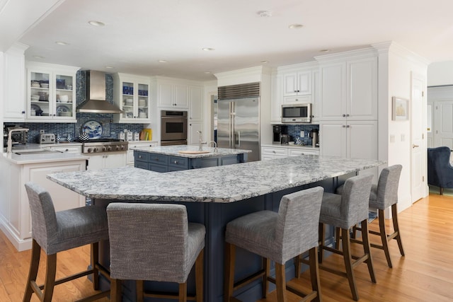 kitchen with a center island with sink, stainless steel appliances, wall chimney exhaust hood, and white cabinets