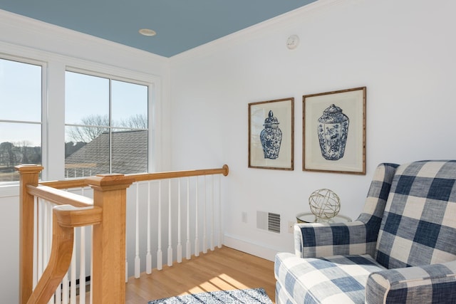 sitting room with an upstairs landing, wood finished floors, visible vents, and ornamental molding