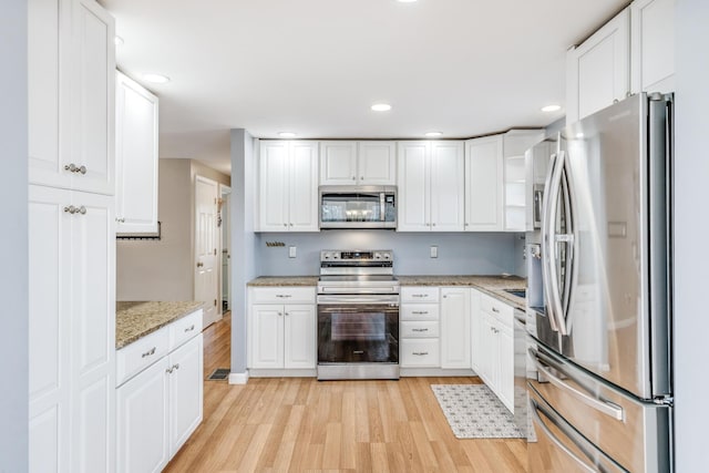 kitchen featuring stainless steel appliances, white cabinets, and light stone counters