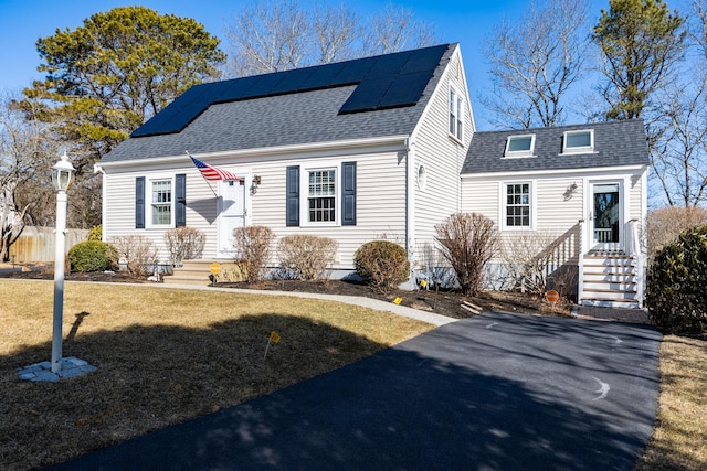 view of front facade with a front yard, roof mounted solar panels, and roof with shingles