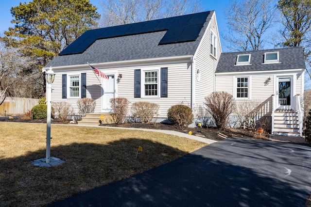 view of front of home with entry steps, a shingled roof, fence, roof mounted solar panels, and a front lawn