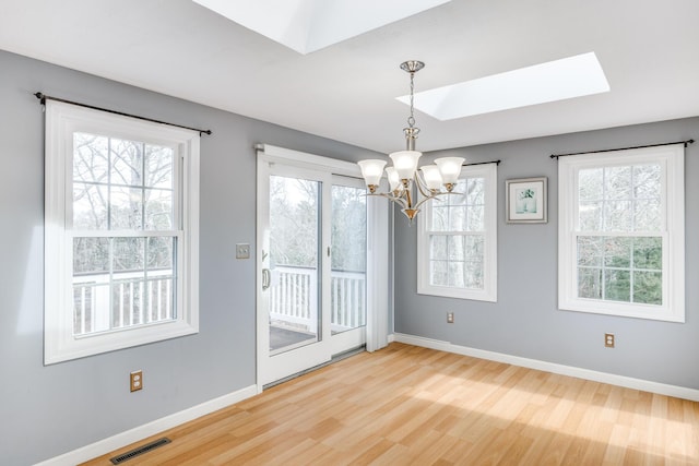 unfurnished dining area featuring a skylight, a notable chandelier, visible vents, wood finished floors, and baseboards