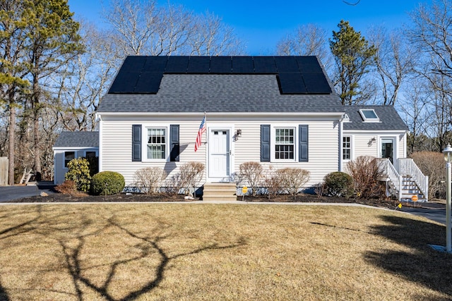 view of front of property with entry steps, a front lawn, solar panels, and roof with shingles