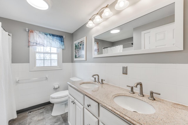 bathroom featuring toilet, double vanity, visible vents, and a sink