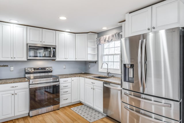 kitchen with stainless steel appliances, a sink, white cabinets, light wood-type flooring, and open shelves