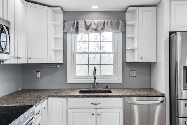 kitchen featuring dark countertops, appliances with stainless steel finishes, white cabinetry, open shelves, and a sink