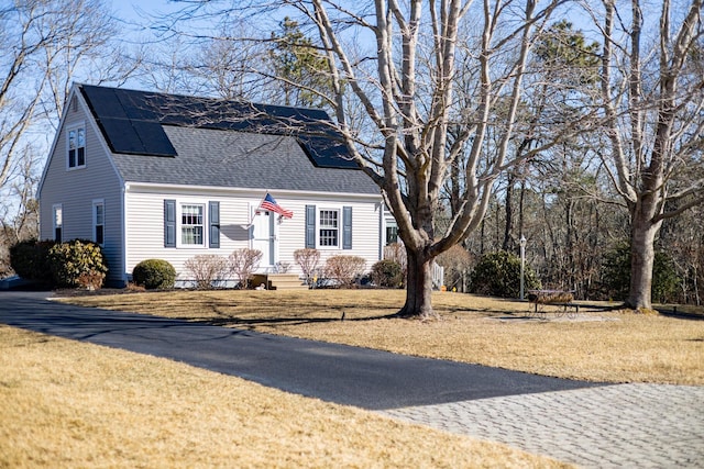 new england style home featuring solar panels, a shingled roof, and a front yard