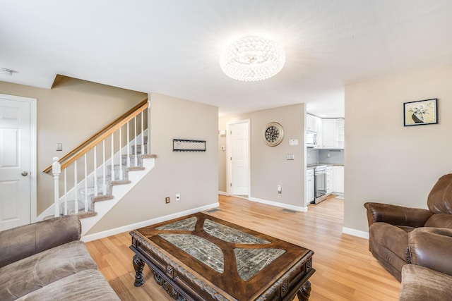 living area with light wood-style flooring, visible vents, stairway, and baseboards