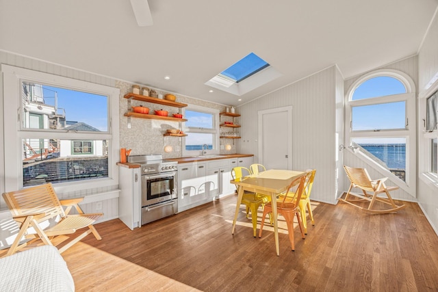 kitchen featuring sink, stainless steel stove, white cabinets, a skylight, and light hardwood / wood-style floors