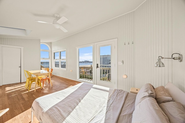 bedroom with ceiling fan, wood walls, access to outside, and hardwood / wood-style flooring