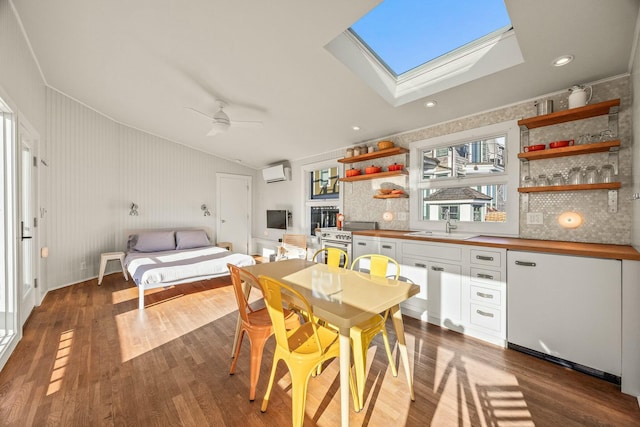 interior space with a wall mounted air conditioner, sink, lofted ceiling with skylight, dark hardwood / wood-style flooring, and ceiling fan