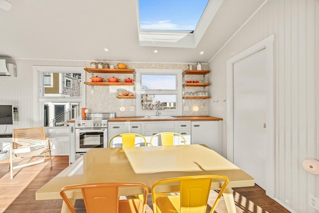 kitchen with stainless steel range, white cabinetry, a skylight, wood walls, and light hardwood / wood-style flooring