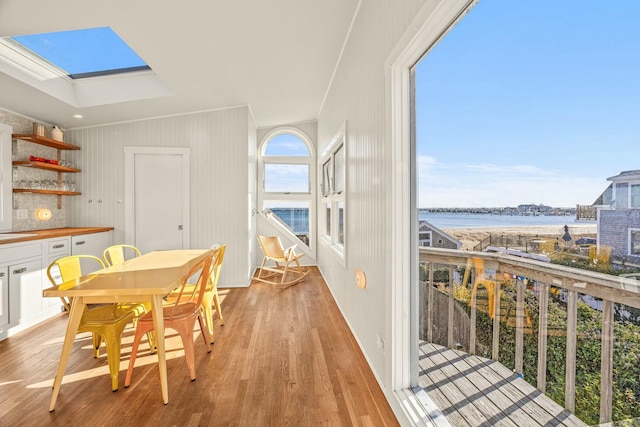 dining room featuring light wood-type flooring, a skylight, a water view, and sink