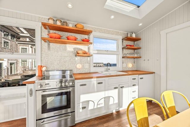 kitchen featuring sink, stainless steel stove, white cabinetry, and butcher block counters