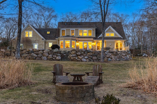 back house at dusk featuring a fire pit and a lawn