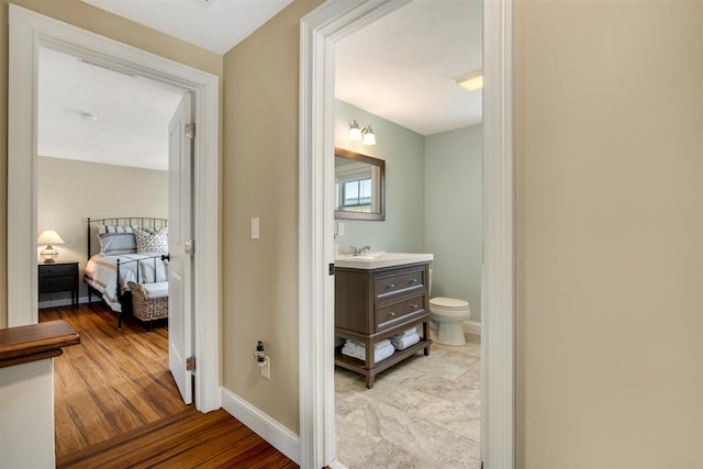 hallway with visible vents, a sink, baseboards, and wood finished floors