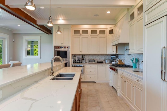 kitchen featuring appliances with stainless steel finishes, decorative light fixtures, beamed ceiling, sink, and light stone counters