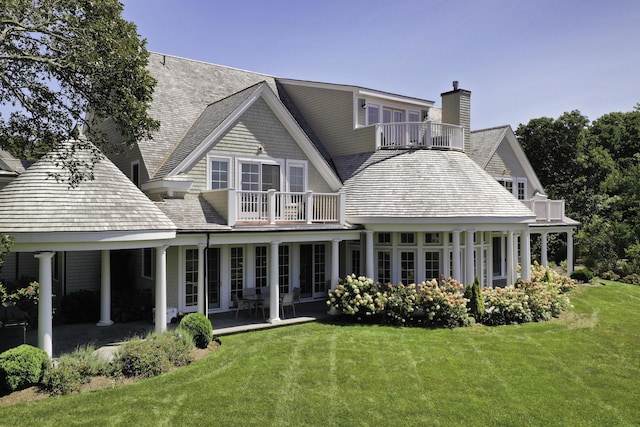 rear view of house with a balcony, a patio area, and a lawn