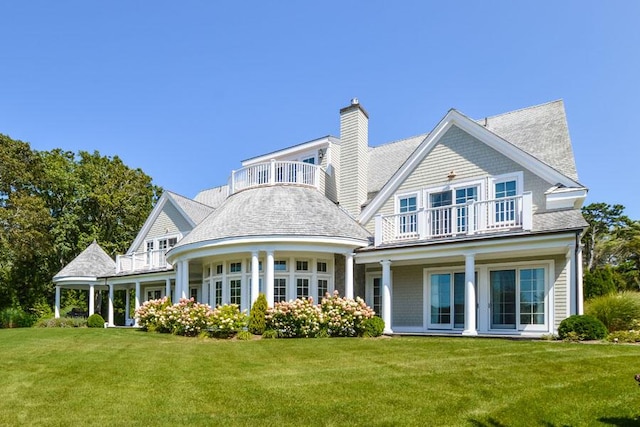 back of property featuring a balcony and a lawn