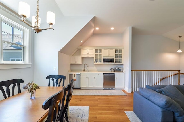 dining area with sink, light wood-type flooring, a chandelier, and vaulted ceiling