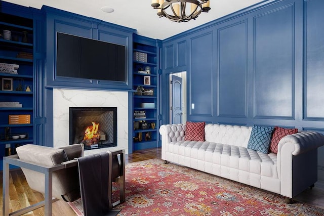 living room with built in shelves, an inviting chandelier, a fireplace, and dark hardwood / wood-style flooring