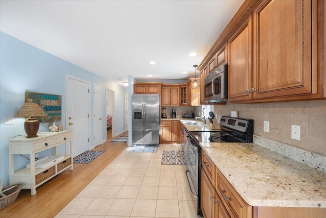 kitchen with stainless steel appliances, tasteful backsplash, brown cabinetry, glass insert cabinets, and light stone countertops