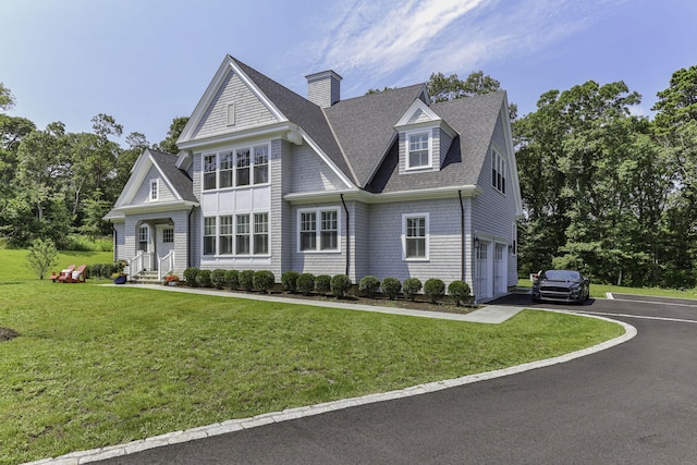 shingle-style home with entry steps, aphalt driveway, a front yard, a shingled roof, and a garage