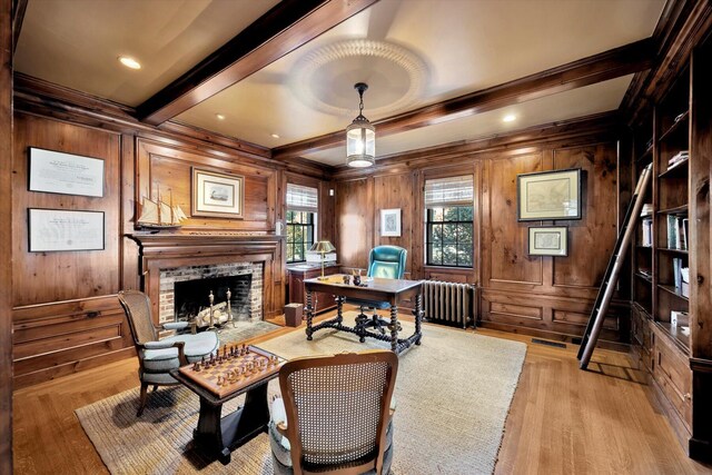 office featuring radiator, a fireplace, wooden walls, beam ceiling, and light hardwood / wood-style flooring